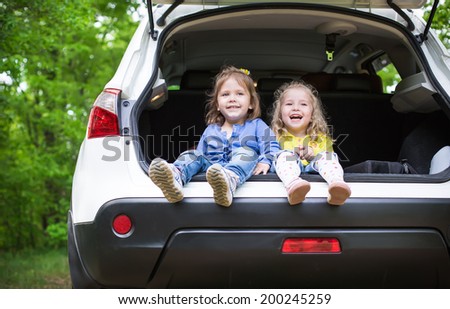 laughing toddler girls sitting in the car in the forest