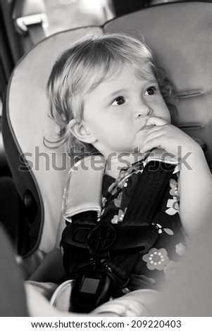 Cute baby sucks his finger sitting in the car seat  ( black and white )