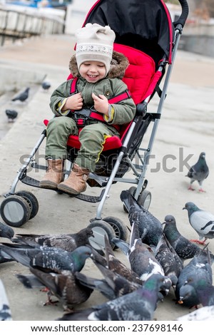 Toddler laughing baby in the stroller looks at pigeons