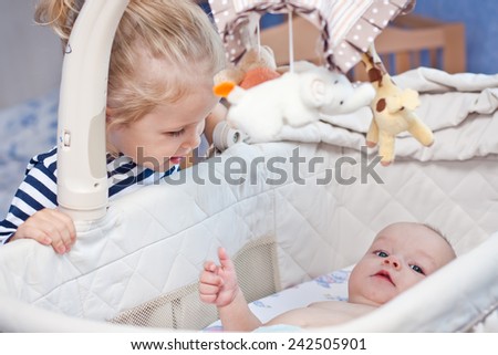 happy little sister looks into the cradle to the newborn brother
