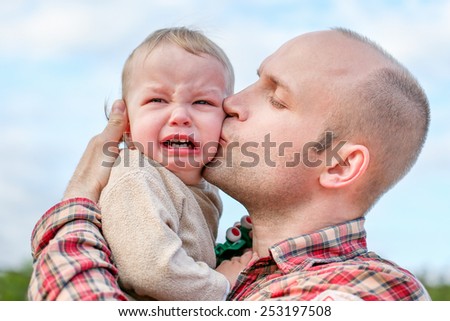 caring father calms toddler son outdoors on the sky background