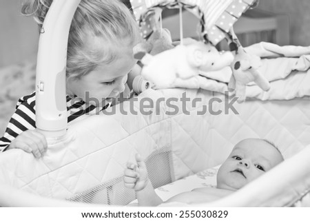happy little sister looks into the cradle to the newborn brother  ( black and white )