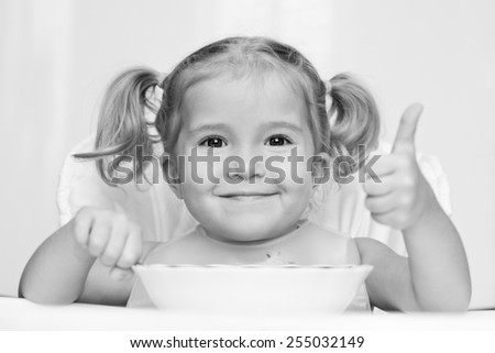happy little girl eats with a spoon while sitting at table ( black and white )