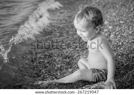 Happy toddler boy playing on the sea at sunset ( black and white )