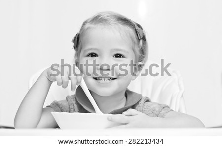 happy little girl eats with a spoon while sitting at table ( black and white )