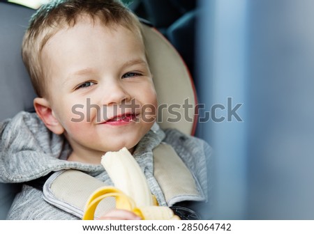 Happy Toddler boy eating a banana in the car