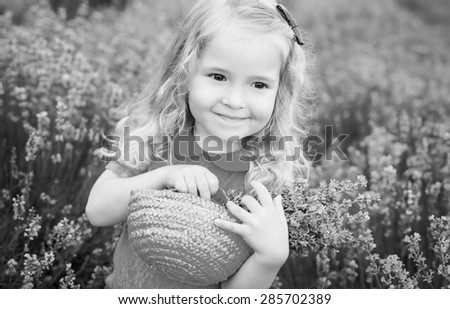 happy little girl is in a lavender field holds a basket of flowers  ( black and white )