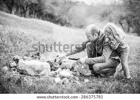 Camping: Dad shows little daughter how to make a fire  ( black and white )