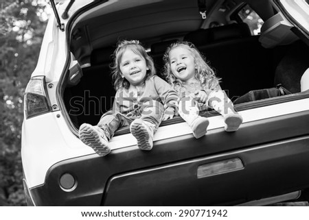 laughing toddler girls sitting in the car in the forest ( black and white )