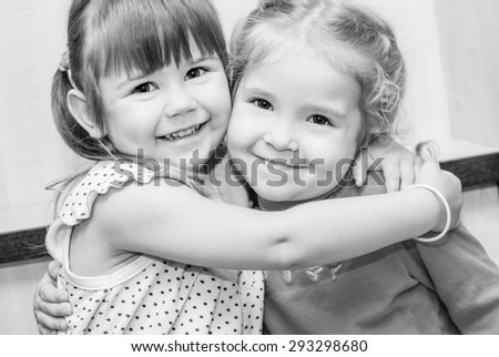 Two happy little girls hugging in the room ( black and white )