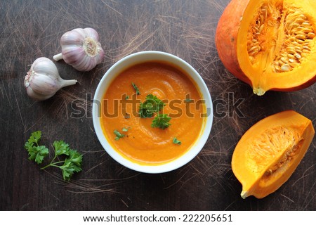 Pumpkin soup in a bowl with fresh pumpkins, garlic and parsley herbs
