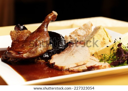 Set of duck leg, sausages, pork slice, cabbage, sauce and two types of dumplings served on white plate
