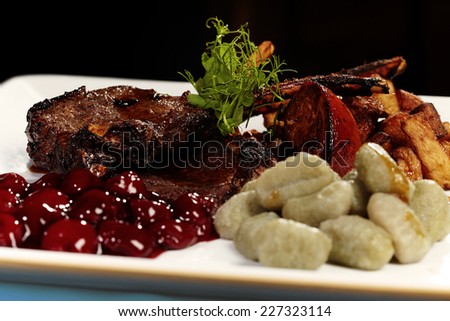 Delicious tender lamb chop with pickled cherries, basil gnocchi and fried potatoes served on plate