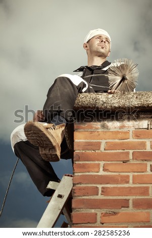 Chimney sweep man in uniform sitting on brick chimney