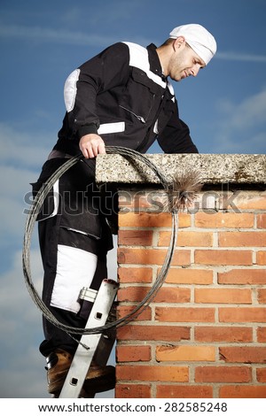 Chimney sweep man in work uniform cleaning brick style chimney