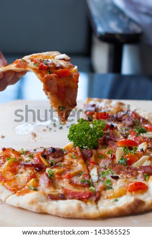 Pizza with bacon, garlic , dried chilli and slice of pizza in hand