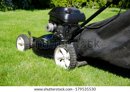 Gas powered lawn mower cutting grass. Black lawn mower left side profile