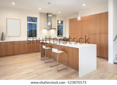 Amazing new contemporary wooden Kitchen with kitchen Island and bar chairs at night.
