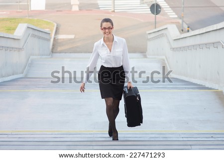 Portrait of a young business woman climbing steps with trolley