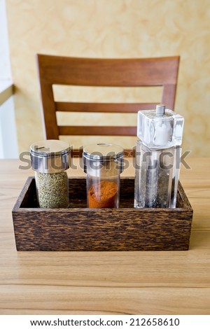 Assorted ground spices in glass bottles in wooden tray on wooden table background.