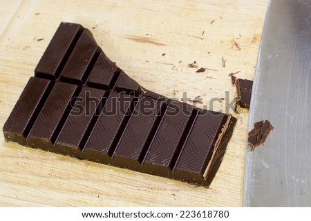 Cut Chocolate bars and knife on a wooden cutting board