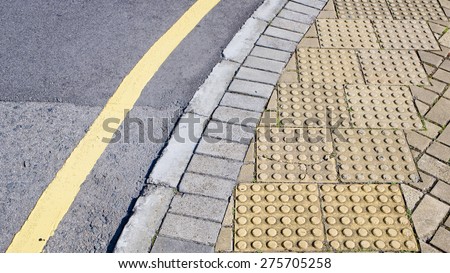 Street curve and yellow curb. Suburban road curve turning right bordered by painted yellow curbs. Textured grey asphalt lined with cracks. Yellow dot brick block on side of the street.