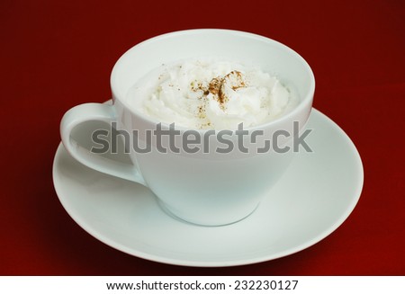 Cup of cappuccino with whipped cream and cinnamon on a red background.