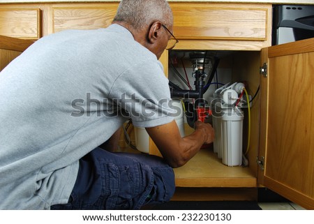 Male senior citizen using a pipe wrench to tighten up pipes under kitchen sink.