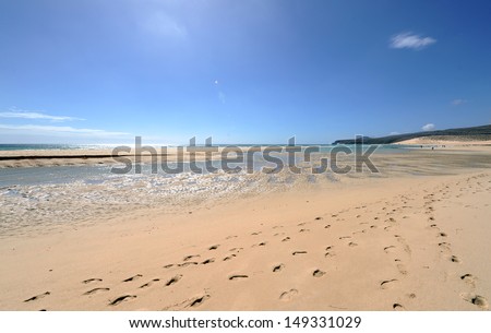 Fuerteventura, Canary islands. Sand beach with footsteps in the sand on a sunny day with a rock in the horizon and a lagoon of water.