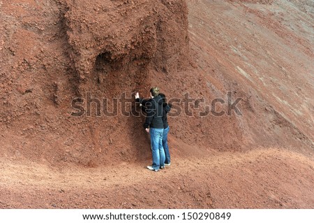 Lanzarote, Canary islands. Two people standing on a path, touching the red rock wall, with their backs facing the camera.