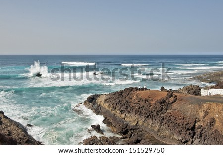 Lanzarote, Canary Islands. A woman and a man standing on a rock, looking at the sea. Waves crushing on rocks in the sea.