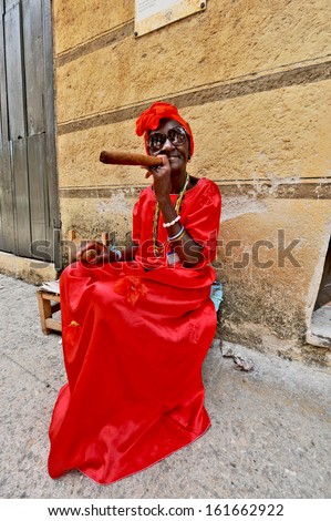 HAVANA, CUBA, MAY 6, 2009. A woman sitting on a bench in the street in a red dress with a huge cigar, in Havana, Cuba, on May 7th, 2009.