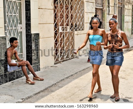 HAVANA, CUBA, MAY 7, 2009. Two beautiful young women walking on a street in Havana, Cuba, on May 7th, 2009. A boy sitting and watching.
