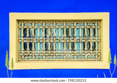 MAJORELLE GARDEN, MARRAKECH, MOROCCO, MAY 11, 2014. A yellow window lattice and window frame in the blue wall of the former house of Yves Saint-Laurent, in Marrakech, Morocco, on May 11th, 2014.