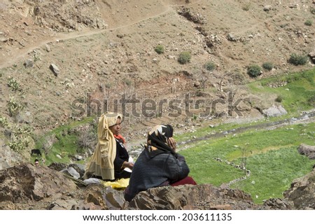 Two Moroccan women dressed in traditional gowns sitting on an edge of a cliff, staring at the valley, in the Atlas mountains of Morocco, on May 13th, 2014.