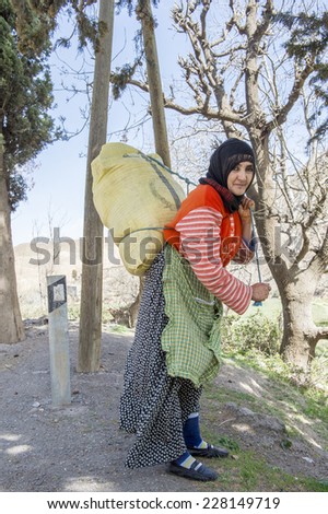 TISLDAY, MOROCCO, MARCH 10, 2014. An old woman with traditional Moroccan clothes and a black headscarf carrying a big bag in her back in Tislady, Morocco, on March 10th, 2014.