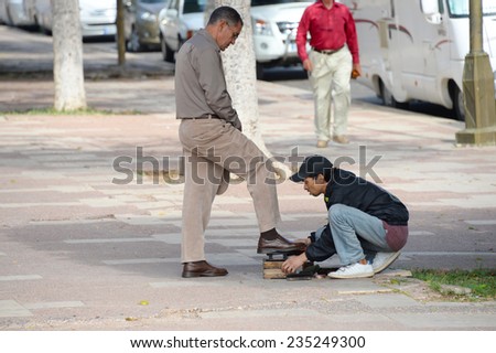 AGADIR, MOROCCO, FEBRUARY 27, 2014. A young Moroccan man shining the shoes of an older Morocaan man in the streets of Agadir, Morocco, on February 27th, 2014.
