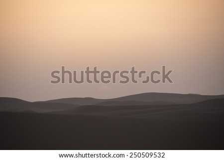 The  sun has fallen behind the horizon. A reddish sky in the Sahara desert in Morocco, with dunes in the front.
