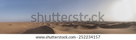 A woman standing alone looking down from the edge of a big sand dune in the Sahara desert in Erg Chegaga in Morocco in the spring during a hot sunny day.