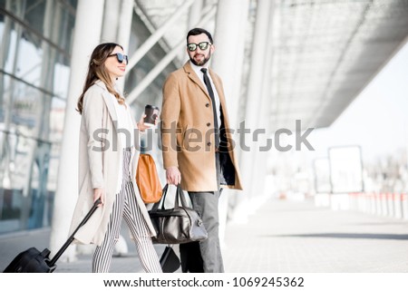 Business couple in coats walking out the airport with luggage during the business trip