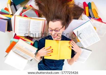 Young and smart girl lying with book surrounded by colorful books on white background
