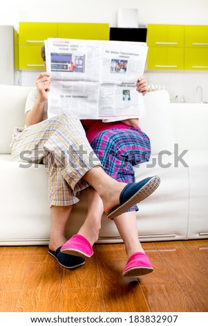 Married couple reading newspaper dressed in pajamas sitting in sofa at home