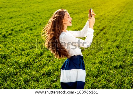 Young and happy woman getting message on the phone on the green field with sunshine