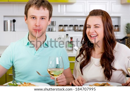 funny couple eating macaroni at the kitchen with wine and salad