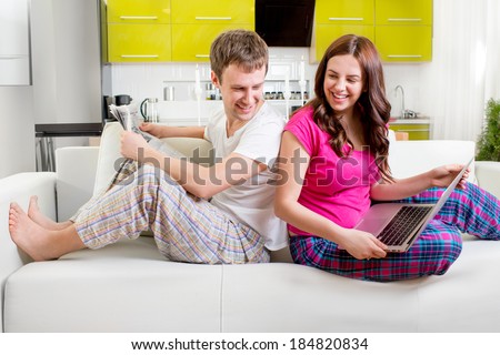 Young married couple in pajamas sitting in the sofa reading newspaper and laughing at home in the morning