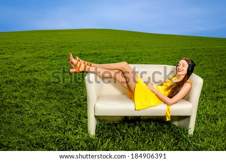 Young girl listening to the music and resting on the couch in the green field