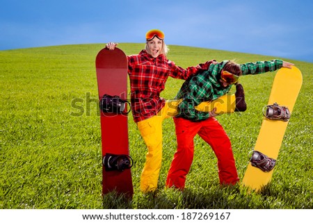 Couple in ski suit having fun with snowboards on the grass in green field