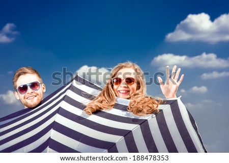 Emotional couple hiding behind the umbrella and having fun on the blue sky background
