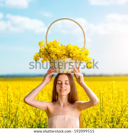 Beautiful happy girl holding the basket full of the yellow flowers on the colza field. Healthy young woman outdoors. Countryside.