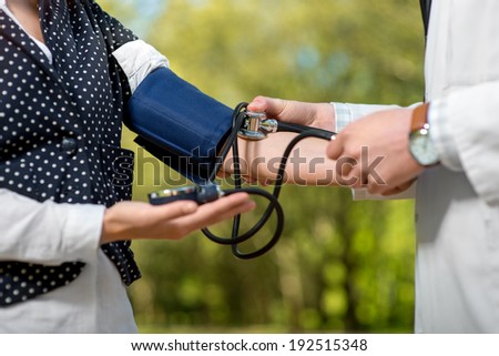Young doctor measuring pressure to young lady in the park. Treatment outdoor, close up plan.